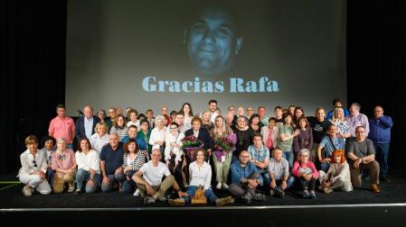 Asistentes al acto con la viuda de Rafa Sánchez sentada en el centro, con el premio, y su madre, justo detrás, con un ramo de flores. De fondo, la imagen del homenajeado.