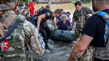 Policías y trabajadores de los servicios de emergencia estatales evacuan a personas de una zona inundada en el río Dnipro en la región de Kherson