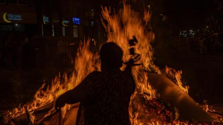 Un hombre tira papeles con sus deseos en la hoguera del barrio de Sant Antoni durante la noche de San Juan en Barcelona