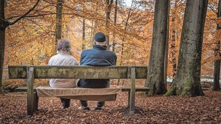 Dos personas mayores descansan en un banco en un paisaje otoñal