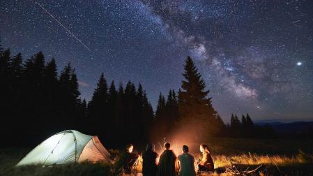 Unos jóvenes contemplan el cielo estrellado durante una acampada