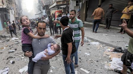 Un hombre sostiene a una niña y a un bebé mientras huye del lugar de un ataque con cohetes israelíes en el campo de refugiados de Al-Shati, en el oeste de la ciudad de Gaza