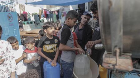 Varios niños palestinos del campamento de Khan Yunis hacen cola para llenar recipientes con agua de un camión cisterna en el sur de la ciudad de Gaza