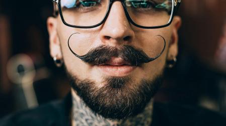Un joven mira a la cámara con un bigote y perilla./