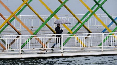 Una mujer con paraguas atraviesa el puente de San Sebastián en Avilés este martes lluvioso