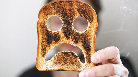 Una persona sujeta una tostada de pan de molde quemada con una cara triste./