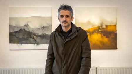Javier Egiluz, posando junto a dos de sus obras en La Fábrica de Gomas. Los negros, grises y ocres son los colores protagonistas