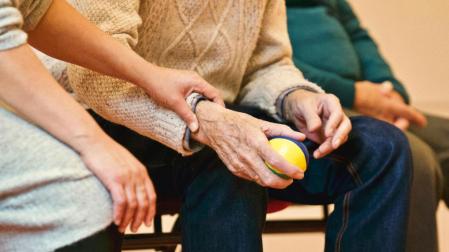 Una monitora ayuda a una persona de la tercera edad a realizar una actividad con una pelota