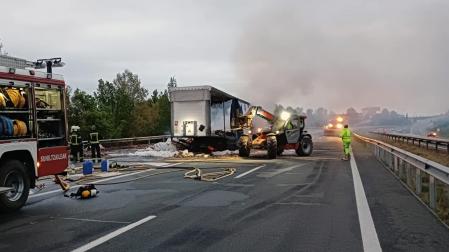 Efectivos de bomberos trabajan junto al camión que se ha incendiado este miércoles por la mañana en la A-15