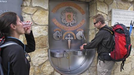 Dos peregrinos refrescan su trayecto del Camino de Santiago en la fuente de las Bodegas Irache