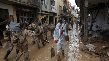 Un grupo de voluntarios pala en mano se cruza con efectivos del ejército en una de las calles de Paiporta, aún anegadas de barro.