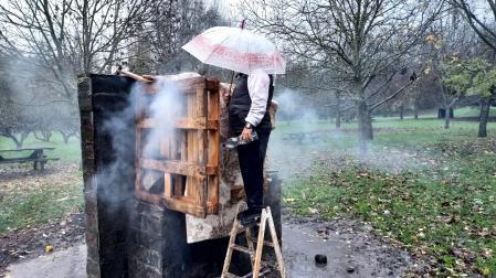 Christian Constantin se protege con un paraguas de la lluvia y echa agua sobre la chimenea artesal que se construyó en un merendero de Huarte