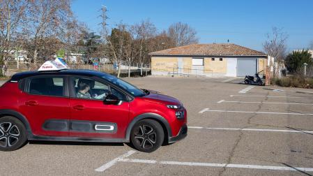 Un coche de autoescuela, con el aula de exámenes, al fondo /