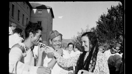 Una joven baztanesa da fuego a un herido con el brazo en cabestrillo, a las puertas del hospital de sangre de Lekaroz, a principios de septiembre de 1936. Al fondo, en la fachada del edificio, ondea una bandera con la Cruz Roja