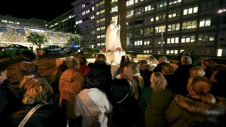 Varias personas rezan por el Papa Francisco justo a la escultura del Papa Juan Pablo II en el hospital donde está ingresado el pontífice