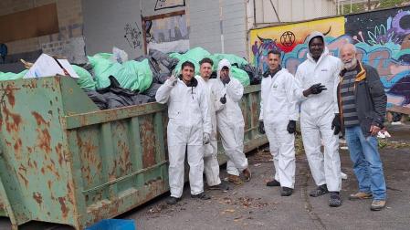 Jóvenes sin hogar introducen en un contenedor la basura recogida del interior del edificio abandonado de la antigua ikastola Jaso en Echavacoiz, donde lvan meses sobreviviendo. A la derecha, Mikel Otazu, profesor jubilado y voluntario de una de las entidades sociales que colaboran en la recogida.