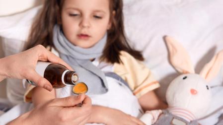 Una persona administra jarabe a una niña