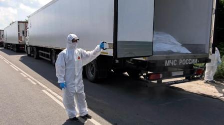 Un oficial con traje de protección contra materiales peligrosos abriendo un camión, parte de un convoy con 1.212 cadáveres de militares ucranianos fallecidos para ser repatriados