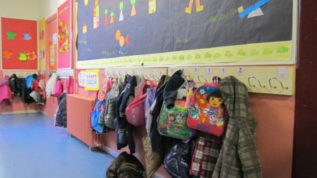Mochilas y ropa en el perchero de un aula infantil.