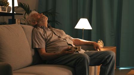 Un hombre mayor se queda dormido en el sofá con el mando de la tele en la mano