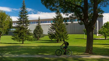 Un estudiante circula por el campus de la Universidad de Navarra con el edificio Amigos al fondo