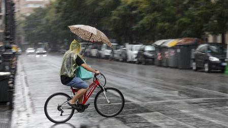 Un hombre circula en bicicleta bajo la lluvia en Valencia