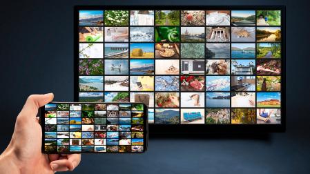 Una persona sujeta un mando móvil con la programación de la televisión, proyectada en la pantalla.