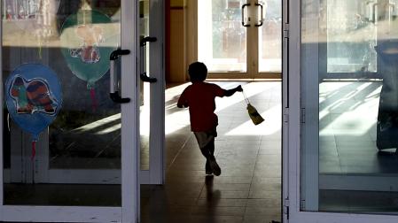 Un niño atraviesa la puerta del colegio con la bolsa del almuerzo en la mano