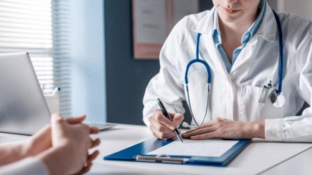 Un médico escucha a un paciente en consulta mientras apunta lo que le va contando