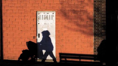 Una mujer empuja una silleta de bebé y su sombra se proyecta en la fachada de la pared de una bajera./