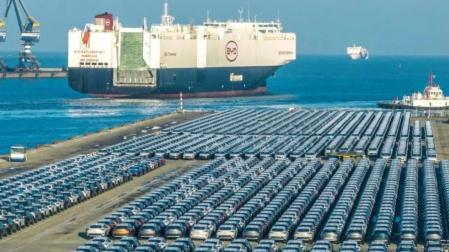 Un megabuque de BYD sale de un puerto chino en el que centenares de coches esperan para su exportación