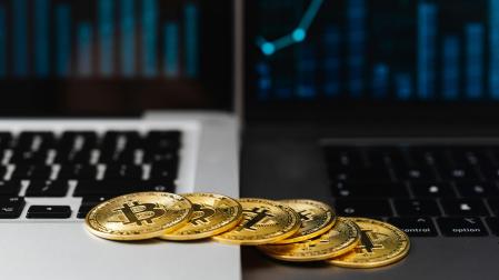 Imagen de recurso de seis bitcoins físicos sobre dos ordenadores, representan el símbolo del bitcoin real, que está en la red.