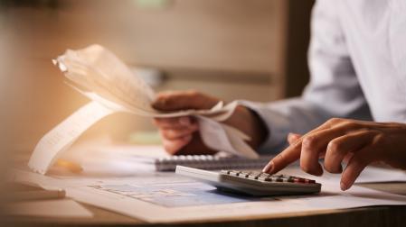 Primer plano de un economista que usa una calculadora mientras revisa las facturas y los impuestos en la oficina