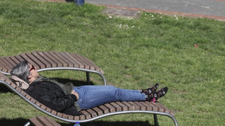 Una mujer toma el sol en un parque en el inicio de la primavera