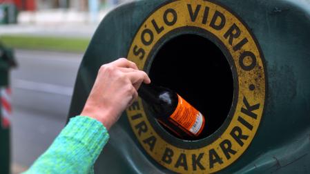 Una personas introduce una botella de cristal en un contenedor en Pamplona.