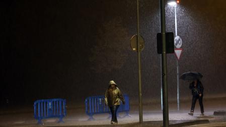 Dos personas caminan bajo la lluvia en Pamplona durante las tormentas de este sábado