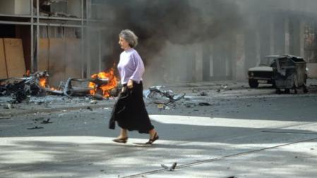 Una mujer corre ante un edificio bombardeado en Sarajevo