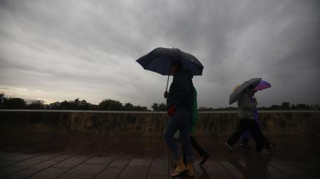 Unas personas tratan de protegerse de la lluvia y de las rachas de viento en Córdoba /