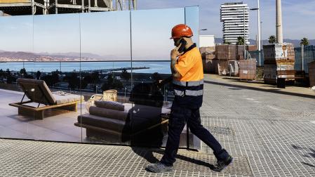 Un operario ante una publicidad de viviendas de lujos con las Torres de Málaga al fondo /
