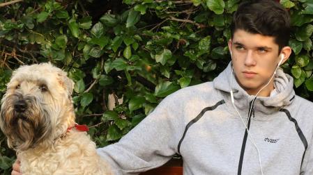 Un adolescente sentado en un banco con su perro mientras lo acaricia