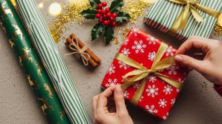 Manos envolviendo un regalo de Navidad con papel rojo y un lazo dorado