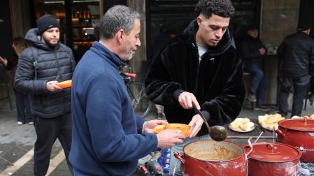 Un voluntario sirve un plato de comida caliente a una persona, este 23 de diciembre en la plaza del Ayuntamiento de Pamplona.