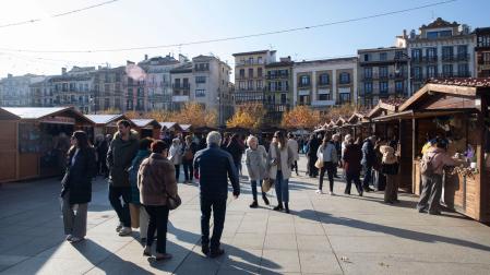 Varias personas paseando entre los puestos de la Feria de Navidad de Pamplona instalada en la plaza del Castillo