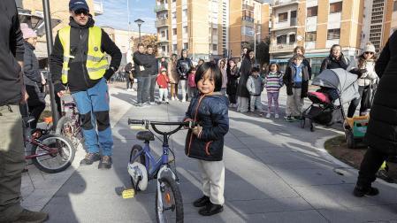 Un niño posa con la bici que le entregó Recicleta, con numerosas personas esperando que les tocara el turno para recibir la suya