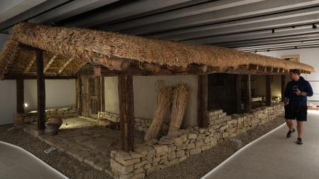 Un visitante observa la reconstrucción, a escala real, de la vivienda donde se halló la Mano de Irulegi. En el dintel  de la puerta de la casa (izq.) se ha colocado una réplica de la Mano.