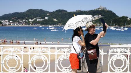 En una imagen de archivo, Una pareja de turistas se protege del sol junto a la playa de La Concha de San Sebastián.