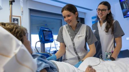 Una enfermera especializada, junto a una estudiante de Enfermería, atienden a una paciente hospitalizada en la planta de Oncología de la Clínica Universidad de Navarra