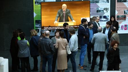 Parlamentarios de otros grupos, en el atrio de la Cámara mientras la pantalla proyecta la intervención en el salón de plenos del portavoz de Vox, Emilio Jiménez