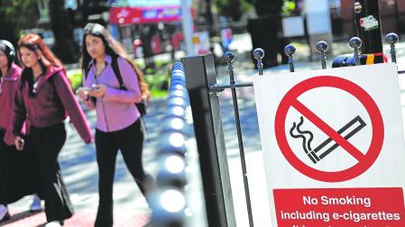 Jóvenes pasan junto a un cartel de ‘prohibido fumar’ frente a una estación de autobuses en el este de Londres