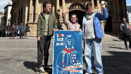 Iosu Zandio, Naiara Olaechea y June Zandio, con su cartel de San Fermín en la plaza del Ayuntamiento de Pamplona
